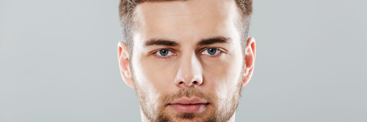 Close up portrait of a young bearded man face looking at camera isolated over gray background